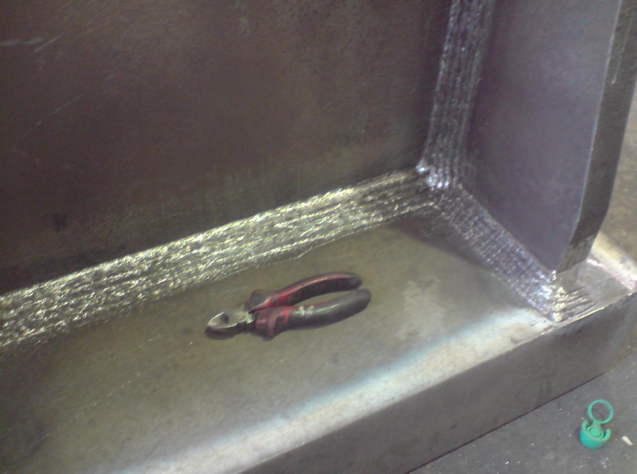 Spoina narożna na grubej, stalowej konstrukcji, obok leżą obcinaczki do drutu z czerwono-czarnymi rękojeściami.