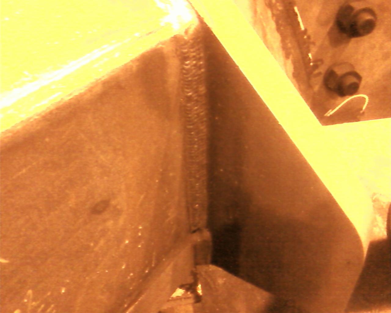 Szczegółowe ujęcie świeżo wykonanego spoiny łączącej elementy stalowej konstrukcji, widoczne ślady obróbki termicznej i mocowania śrubowe.