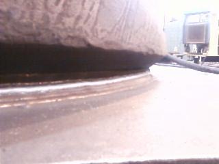 Zbliżenie na spawany element konstrukcyjny, widoczne ślady spawania i nierówności powierzchni, szaro-brązowa kolorystyka, w tle fragmenty konstrukcji i przewód