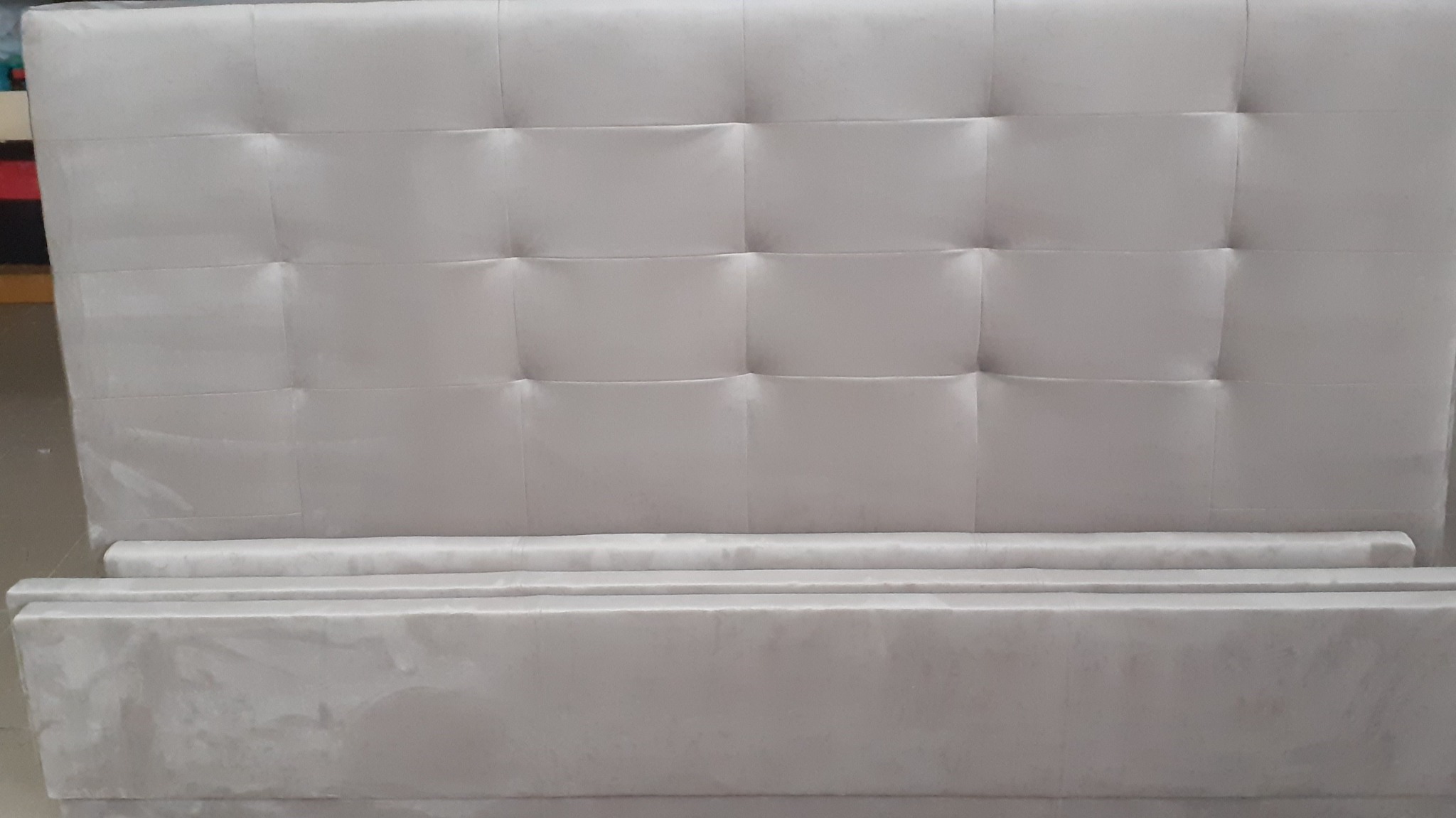 Elementy tapicerowanego łóżka w odcieniach szarości: wezgłowie z kwadratowymi przeszyciami i rama w trakcie montażu.