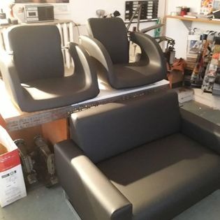 Komplet czarnych mebli tapicerowanych: dwuosobowa sofa i dwa fotele w minimalistycznym stylu, ustawione w warsztacie stolarskim z widocznymi narzędziami i materiałami.