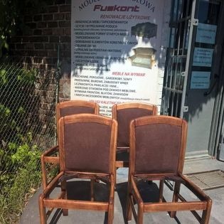 Cztery drewniane krzesła z brązowym obiciem, w trakcie renowacji, bez siedzisk, na tle ceglanej ściany i tablicy informacyjnej warsztatu meblowego FusKont.