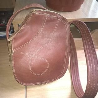 Brązowa skórzana torebka damska z jasnymi przeszyciami, leżąca na blacie mebla, widoczna z góry w lekko rozmytym ujęciu.