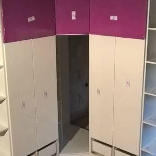 Wnętrze garderoby w trakcie montażu: białe korpusy szaf z fioletowymi frontami w górnej części, widoczne półki po bokach, niedokończone wykończenie, zabezpieczenia na frontach.