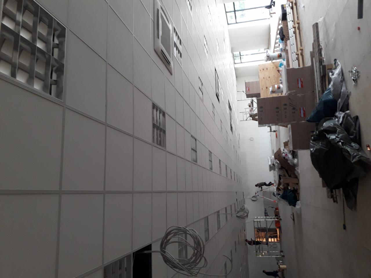 Wysokie pomieszczenie w trakcie montażu ścian działowych z widocznymi elementami konstrukcyjnymi, instalacjami elektrycznymi i materiałami budowlanymi.