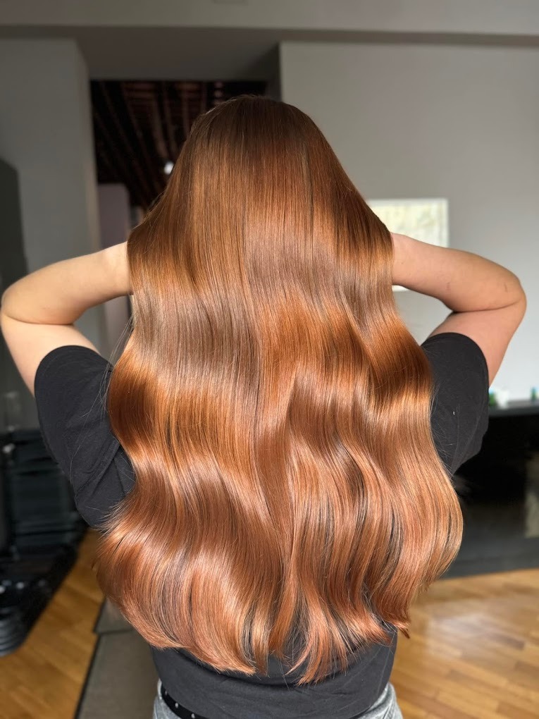 Długie, lśniące, miedziane włosy z delikatnymi falami, widok z tyłu, ręce uniesione do góry, ciemna koszulka.