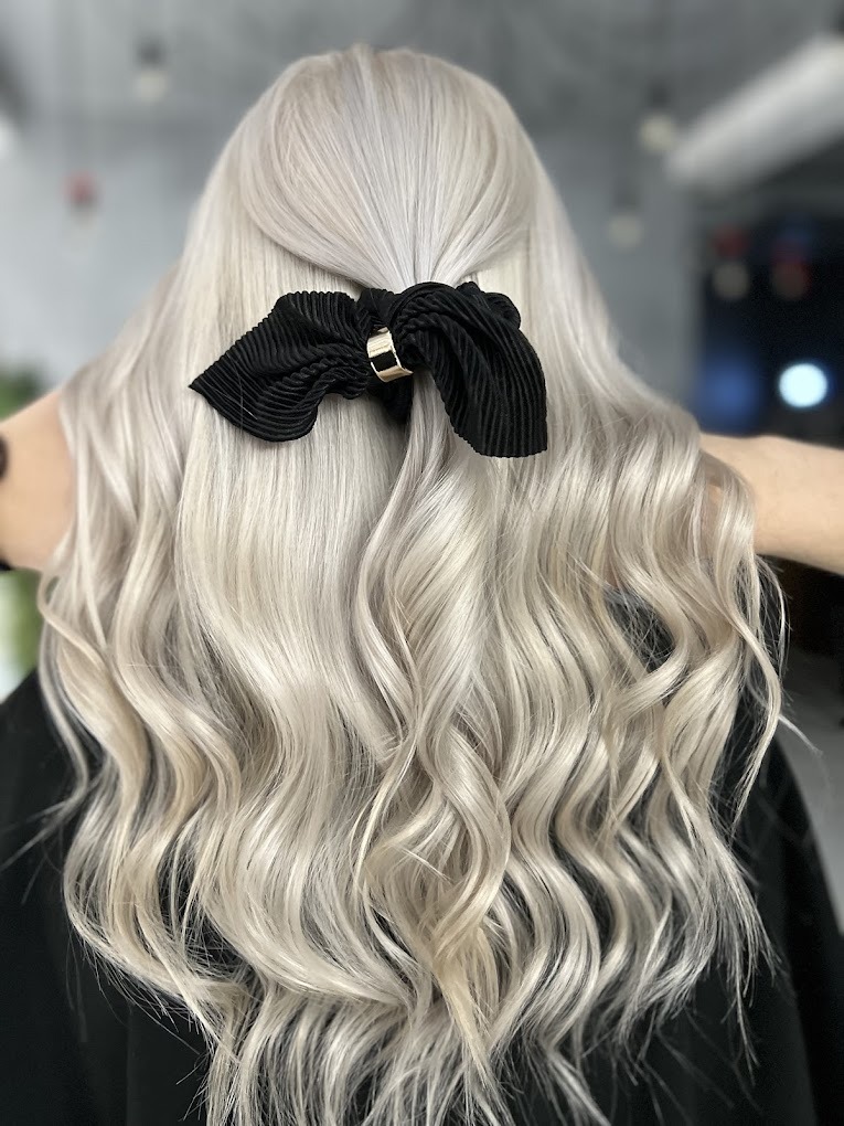 Tył głowy z długimi, platynowymi włosami, delikatnie pofalowanymi i upiętymi czarną, plisowaną kokardą z metalową spinką.