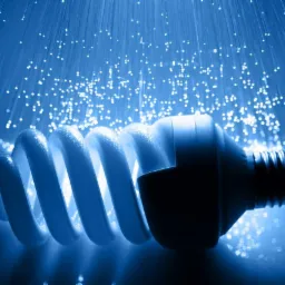 Energooszczędna żarówka spiralna w chłodnym, niebieskim oświetleniu, otoczona światłowodami tworzącymi efekt rozgwieżdżonego nieba.