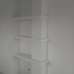 Biała zabudowa z płyt kartonowo-gipsowych tworząca półki w rogu pomieszczenia, świeżo po montażu, widoczne niedoskonałości wykończenia ścian i podłogi.