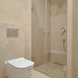 Nowoczesna łazienka w beżowych płytkach z kabiną prysznicową ze szklanymi drzwiami, podwieszaną miską WC i chromowanym przyciskiem spłukującym.