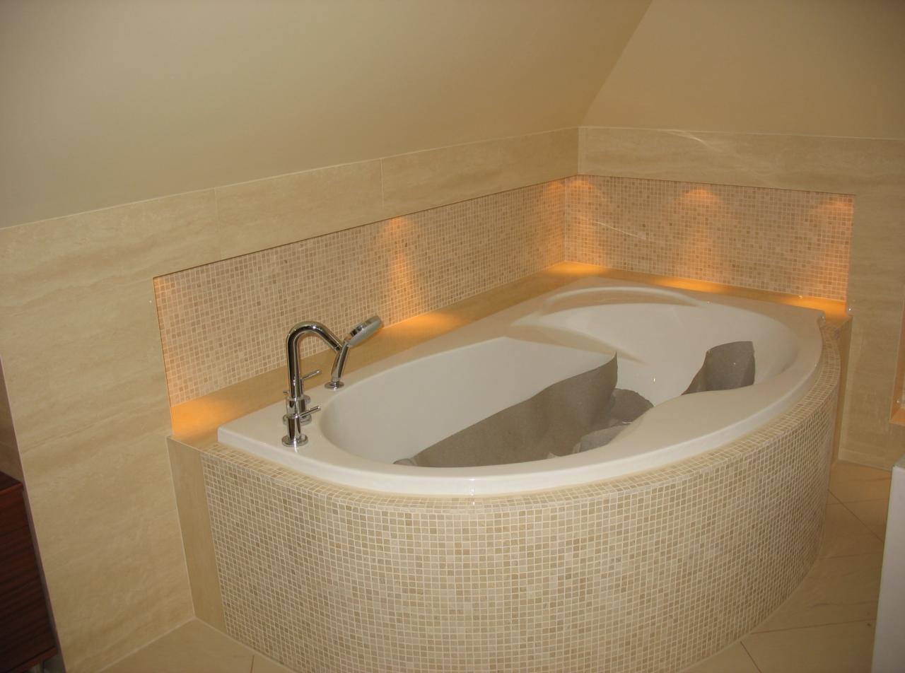 Narożna wanna w obudowie z mozaiki, z chromowaną baterią i podświetleniem LED w niszy ściennej, zabezpieczona kartonem przed zabrudzeniem podczas prac wykończeniowych.