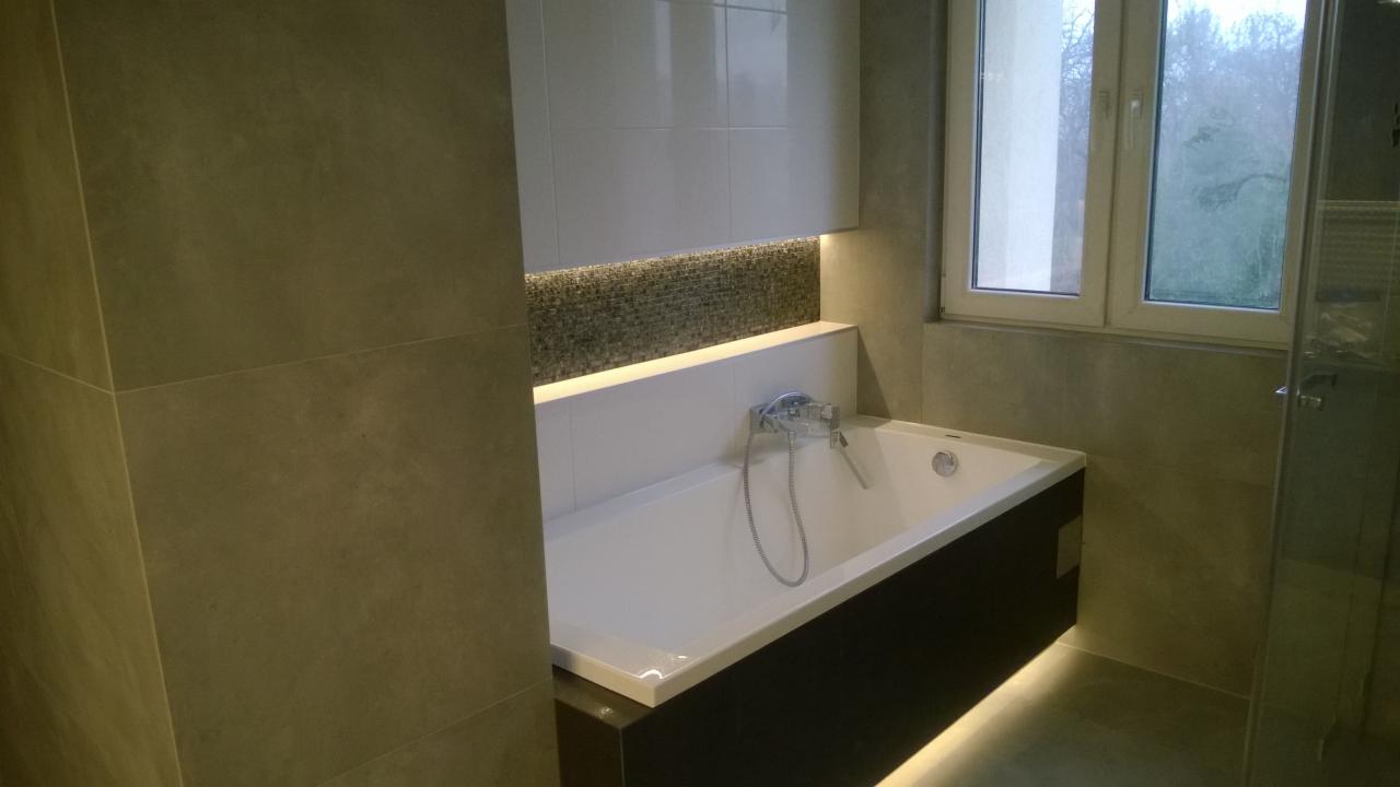 Wykończona łazienka z wanną obudowaną czarnymi panelami, mozaiką nad wanną podświetloną ledami, oraz szarymi płytkami na ścianach i podłodze.