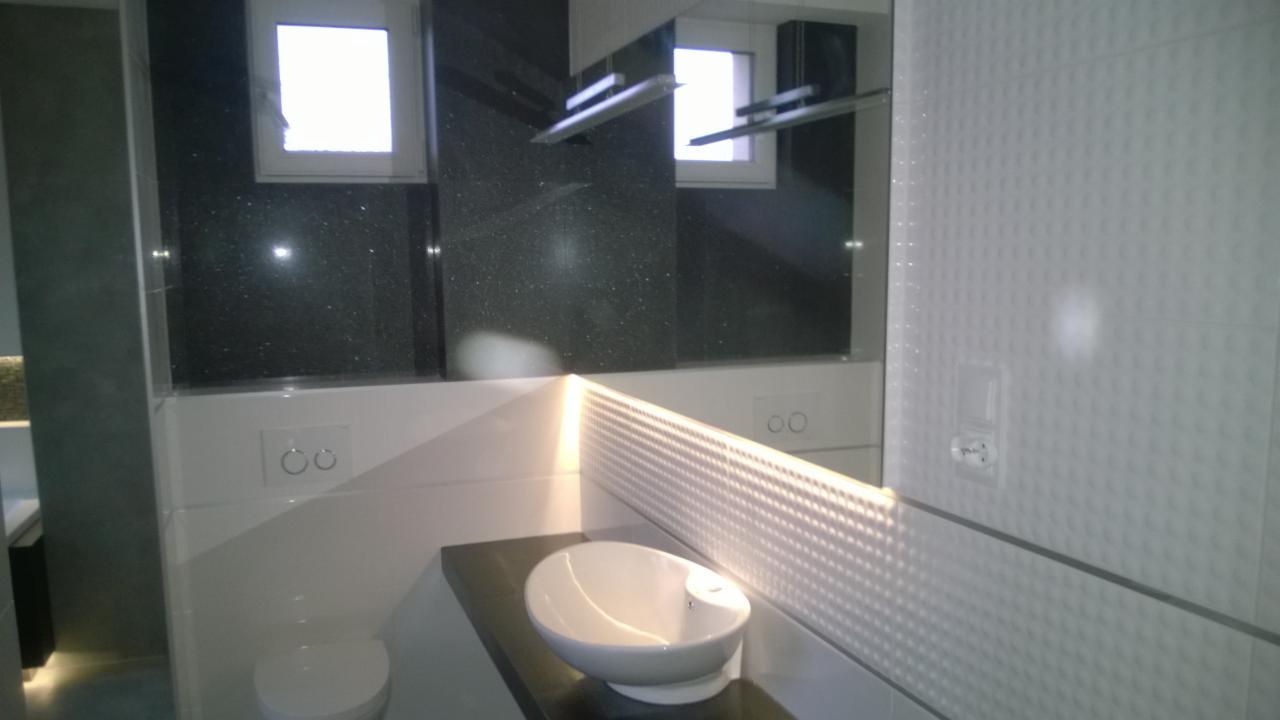 Nowoczesna łazienka z czarnym, błyszczącym granitem i białą, teksturowaną płytką. Umywalka nablatowa i podświetlenie LED tworzą elegancki efekt.