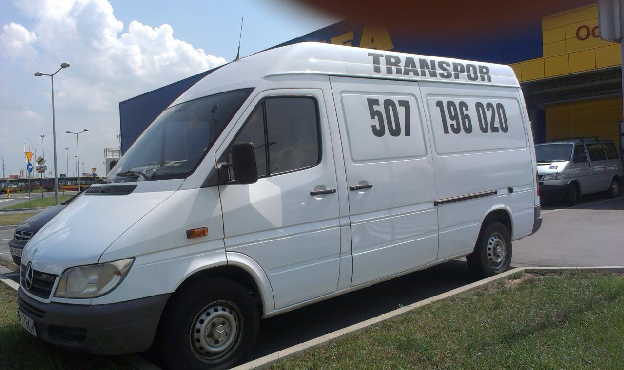 Biały bus transportowy z czarnym napisem 'TRANSPORT' i numerem telefonu 507 196 020, zaparkowany na tle budynku IKEA.