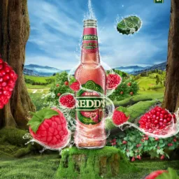 Butelka napoju malinowego Redd's otoczona tryskającą wodą i malinami na tle leśnego krajobrazu z górami w oddali.