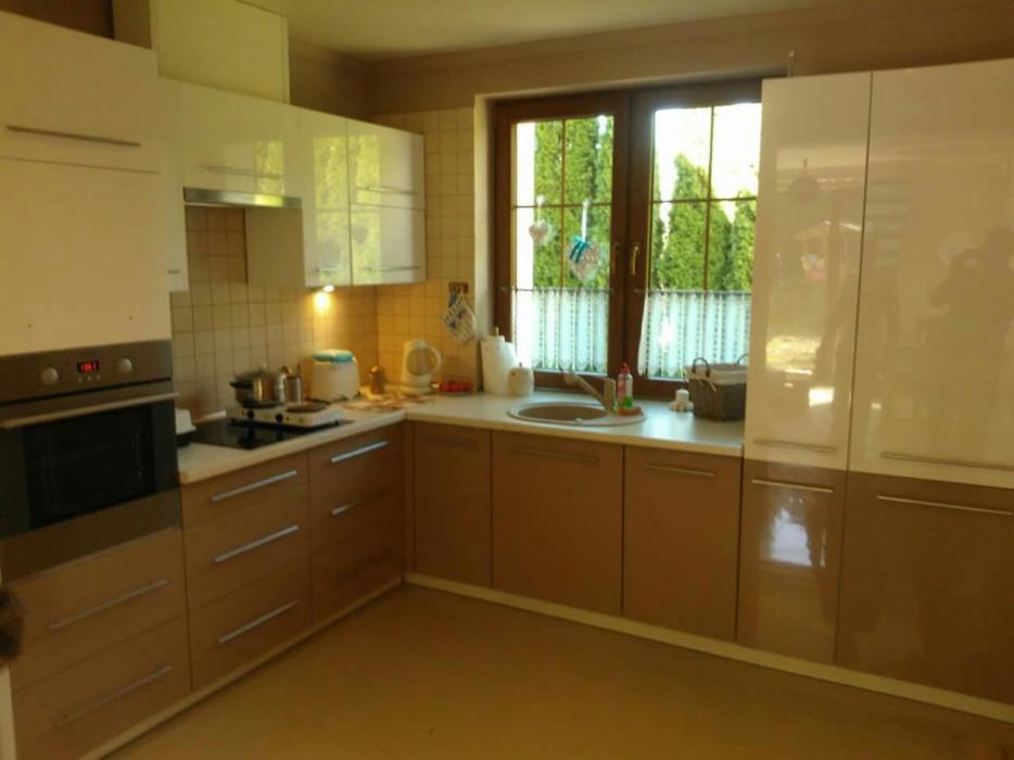 Jasna kuchnia w zabudowie z brązowymi i białymi frontami, widok na okno z firanką i zielenią za nim.