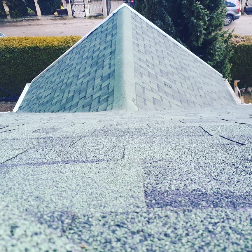 Widok z góry na nowy dach pokryty zielono-szarym gontem bitumicznym, z wyraźnie zaznaczonym kalenicą i widocznymi elementami wykończeniowymi w kolorze białym.