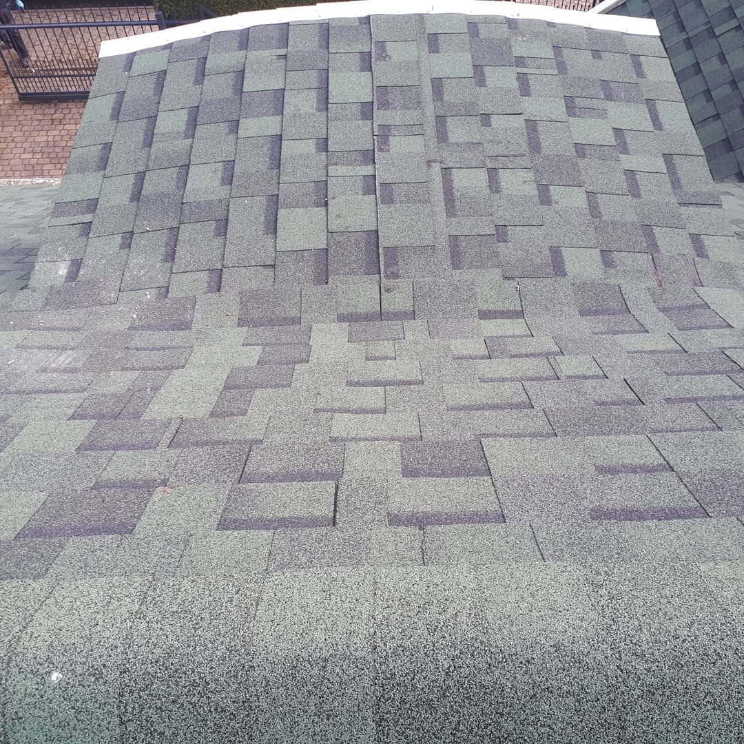 Widok z góry na dach pokryty nowymi, bitumicznymi gontami w odcieniach szarości i zieleni, ułożonymi w regularny wzór. Widoczna struktura i faktura materiału.