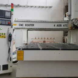 Czteroosiowa frezarka CNC z panelem sterowania, widoczne narzędzia tnące i czujniki na stole roboczym.