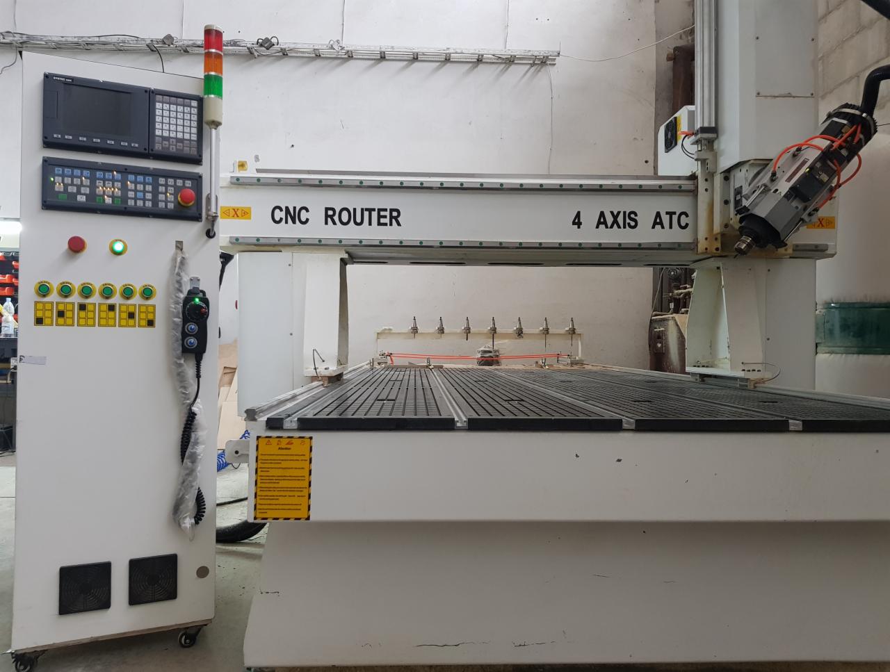 Czteroosiowa frezarka CNC z panelem sterowania, widoczne narzędzia tnące i czujniki na stole roboczym.