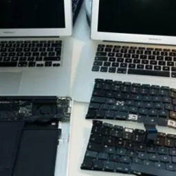 Dwa laptopy MacBook Air, jeden z widoczną klawiaturą, drugi z częściowo zdemontowaną obudową i klawiaturą obok, ukazując wnętrze i komponenty.