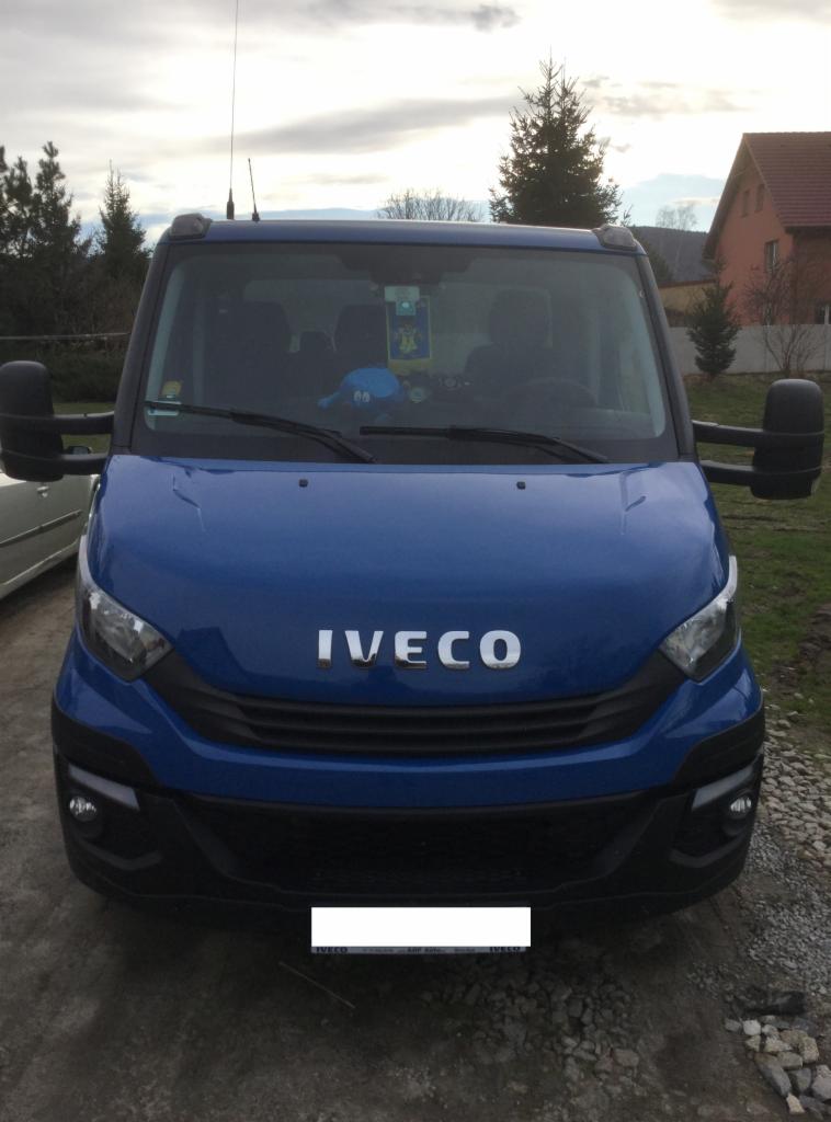 Przód niebieskiego busa marki Iveco z anteną na dachu, zaparkowanego w Grodzisku, z widocznymi ozdobami na przedniej szybie.