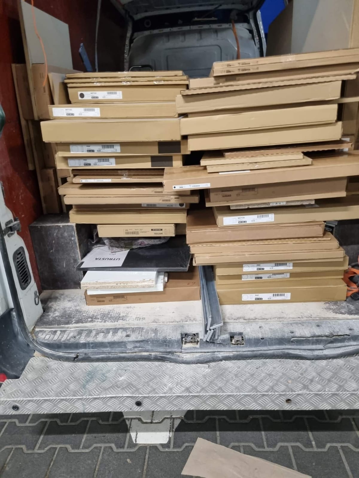 Wnętrze brudnego busa wypełnione po brzegi kartonami i elementami meblowymi, prawdopodobnie z Ikei, widoczne etykiety 'PAX', 'METOD', 'UTRUSTA'.