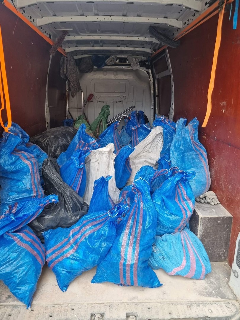 Wnętrze dostawczego auta wypełnione workami z niebieskiej folii z czerwonymi pasami, niektóre worki czarne i białe, po lewej stronie pomarańczowy pas mocujący, ślady brudu na podłodze.