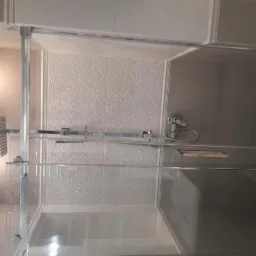 Szklana kabina prysznicowa z deszczownicą i baterią zamontowana na ścianie z ozdobnymi płytkami w łazience.