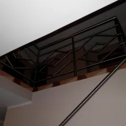 Metalowa balustrada schodowa ze spawanych elementów o geometrycznym wzorze, widok z dołu, oświetlenie sufitowe.