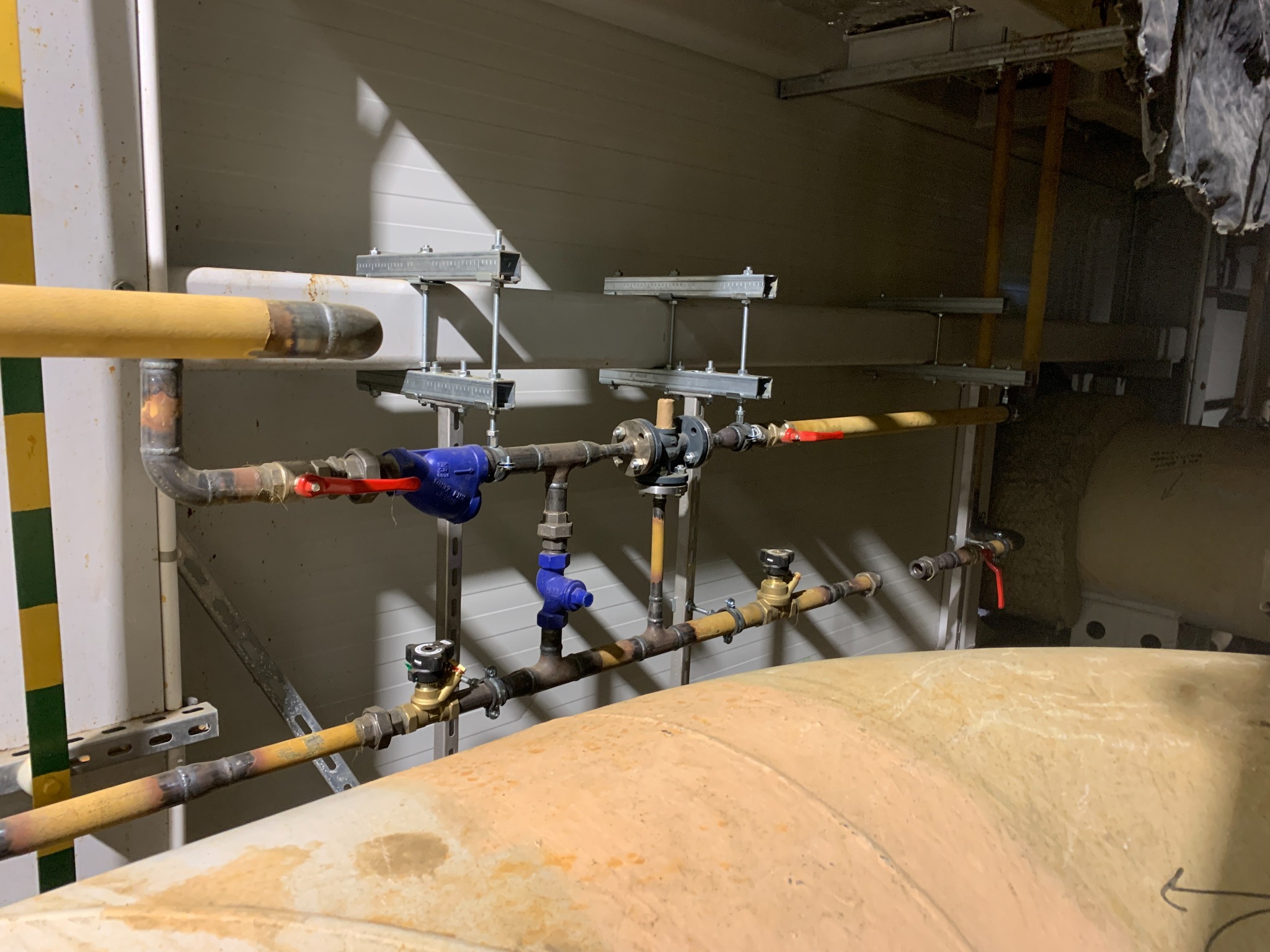 Rurociąg przemysłowy z zaworami i elementami mocującymi, widoczne ślady spawania na rurach, oświetlenie halogenowe.