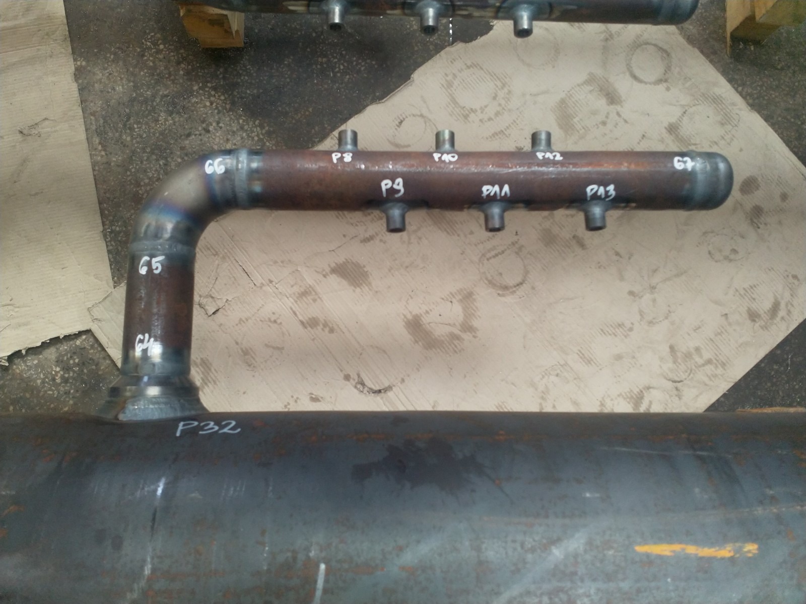 Spawany kolektor rurowy z numeracją punktów spawania, widoczne spawy i oznaczenia na metalu.