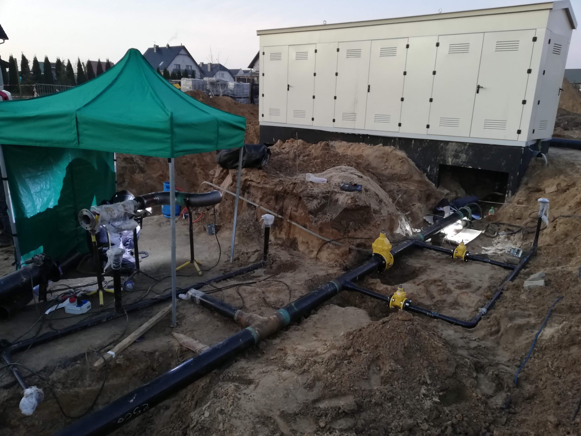 Prace spawalnicze przy łączeniu rur pod ziemią w Strzegomiu, widoczne elementy instalacji oraz sprzęt pod zielonym namiotem.