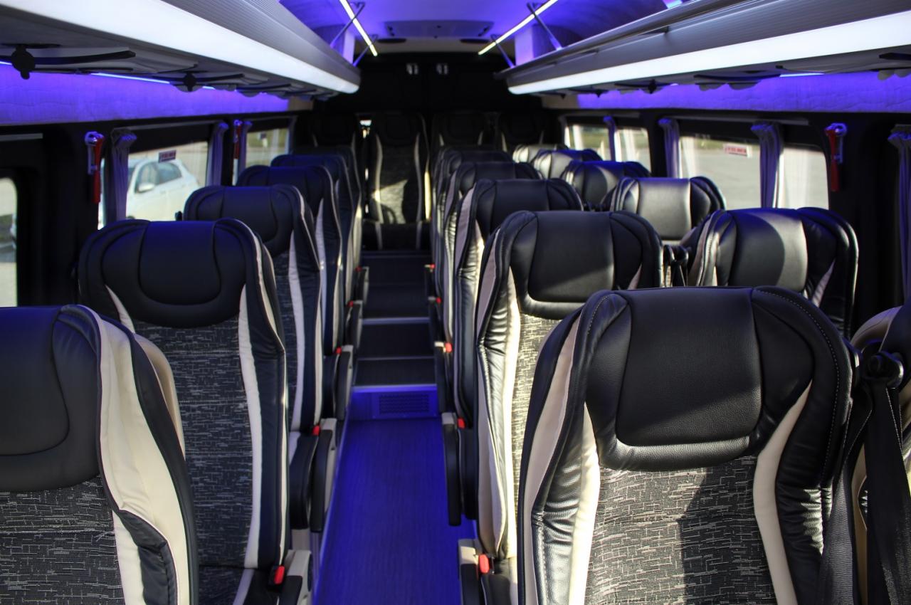 Wnętrze autobusu z rzędami czarno-szarych foteli z jasnymi zagłówkami, oświetlone niebieskim światłem