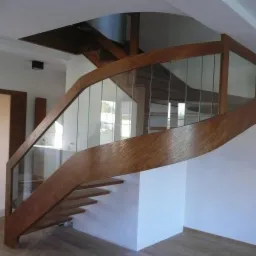 Spiralne schody z drewna z przezroczystymi szklanymi panelami, widoczne z dołu, minimalistyczny design, jasne wnętrze.