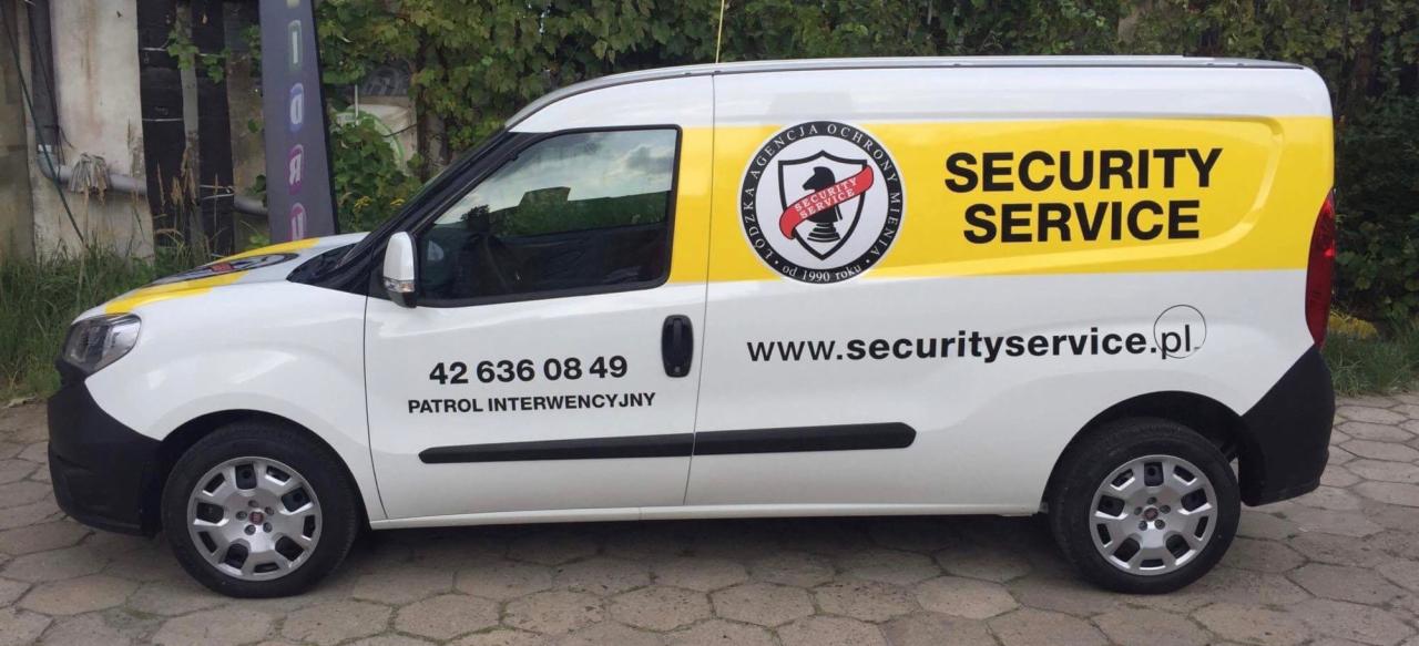 Biały samochód dostawczy z żółtym pasem, oznakowany logo i danymi kontaktowymi do patrolu interwencyjnego.