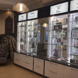 Salon optyczny z ekspozycją okularów marek Gucci, Dior, Chloe, Fendi, Givenchy, Jimmy Choo w podświetlonych gablotach na tle fototapety z motywem miejskim i designerską lampą.