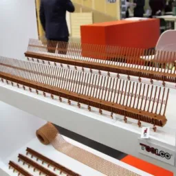 Brązowe grzebienie i siatka do obróbek blacharskich prezentowane na białym regale w Białymstoku, z widocznym logo producenta.