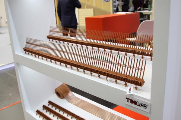 Brązowe grzebienie i siatka do obróbek blacharskich prezentowane na białym regale w Białymstoku, z widocznym logo producenta.