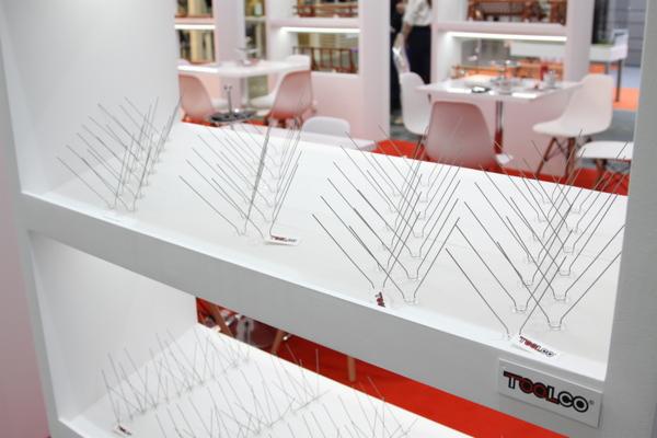 Metalowe kolce przeciw ptakom zamocowane na białych półkach wewnątrz jasnego pomieszczenia, widoczne logo TOOLCO.