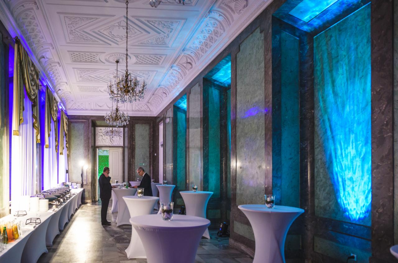 Elegancka sala balowa z bufetem, stolikami koktajlowymi i marmurowymi ścianami podświetlonymi na niebiesko, przygotowana na imprezę integracyjną.