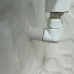 Białe rury kanalizacyjne z uszczelnieniem z konopi, zamontowane na ścianie z dekoracyjną, falistą fakturą płytek.