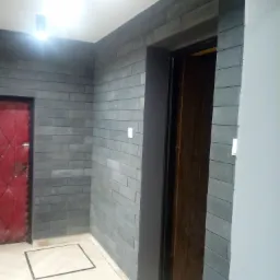 Ściana wyłożona szarymi cegłami w Bielsko-Białej, z widocznymi drzwiami w kolorze bordo po lewej i drewnianymi drzwiami po prawej, oraz jasną podłogą z kwadratową klapą inspekcyjną.