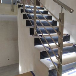 Metlux Rafał Żelazny - Polerowane, metalowe poręcze schodowe z poziomymi prętami, zamontowane na schodach z czarnymi i białymi płytkami. Widoczne zabezpieczenia na schodach.