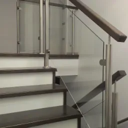 Szklana balustrada schodowa z drewnianą poręczą i słupkami ze stali nierdzewnej, mocowana punktowo do stopni schodów o ciemnym wykończeniu.