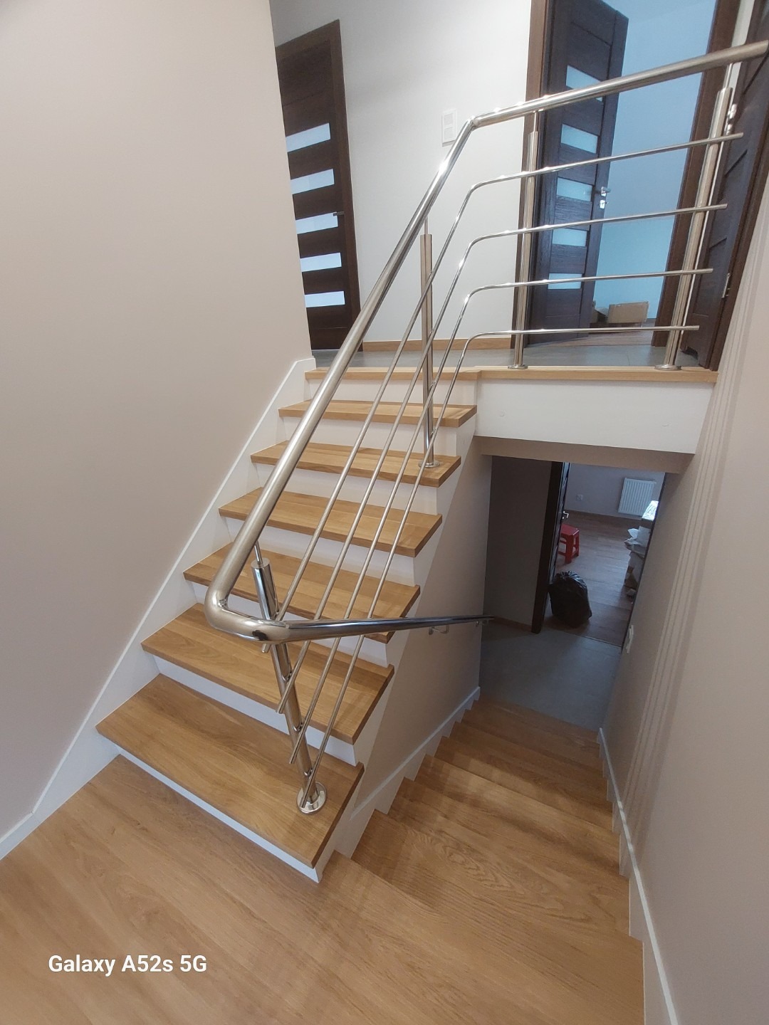 Schody z drewnianymi stopniami i nowoczesną, metalową poręczą. Widok z góry, ukazujący detale wykończenia i estetyczne połączenie materiałów.