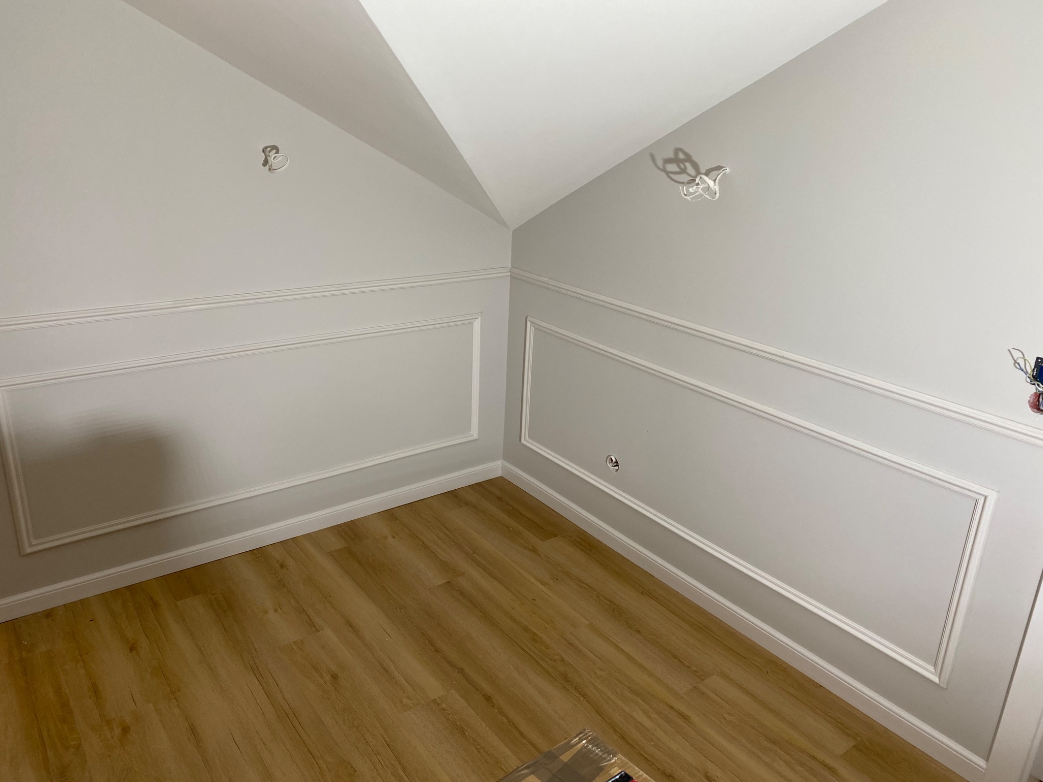 Pokój po remoncie z szarymi ścianami, sztukaterią i panelami podłogowymi, widoczne wystające kable elektryczne.