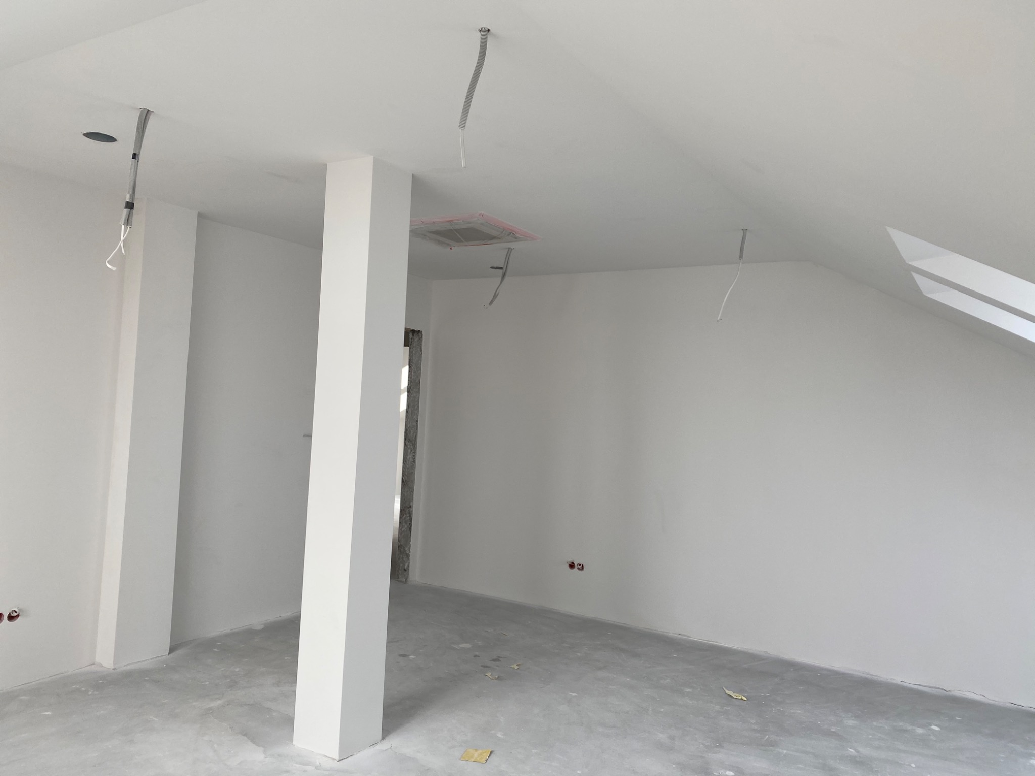 Wnętrze poddasza po szpachlowaniu i malowaniu na biało, widoczne przygotowane kable elektryczne i kratka wentylacyjna zabezpieczona folią.