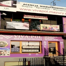 Fioletowa fasada agencji nieruchomości Viva-Pol z szyldami reklamowymi, w oknach oferty nieruchomości oraz numer telefonu kontaktowy.
