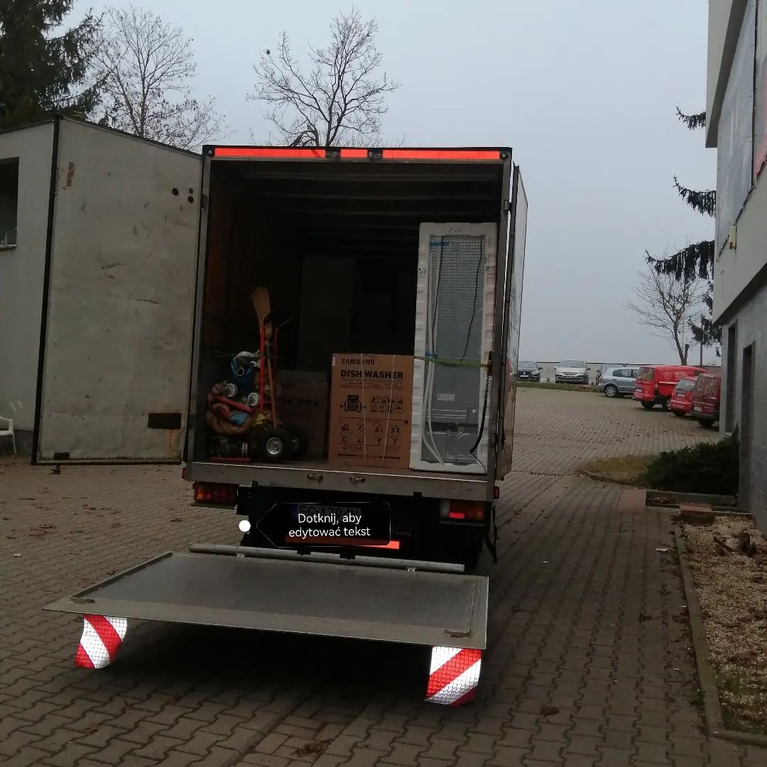 Otwarta paka samochodu dostawczego w Gorzowie Wielkopolskim, załadowana kartonem z napisem Samsung Dish Washer, lodówką w folii i wózkiem transportowym.